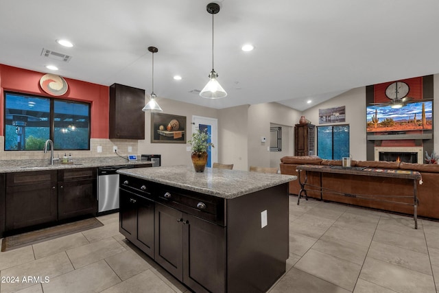 kitchen with tasteful backsplash, light stone counters, sink, decorative light fixtures, and a kitchen island