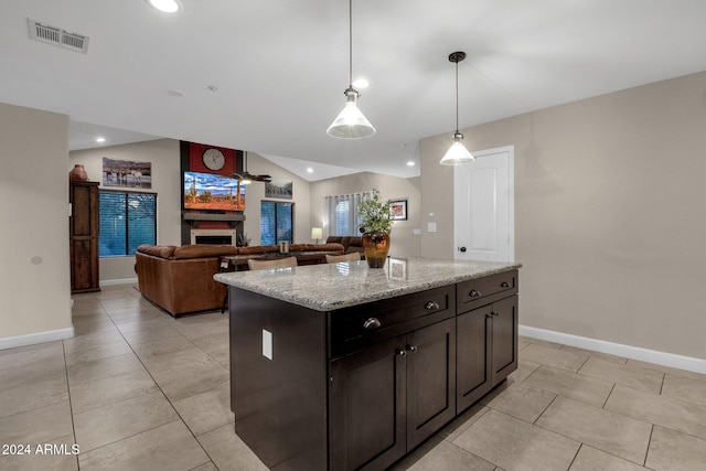 kitchen with a center island, light tile patterned floors, decorative light fixtures, a large fireplace, and light stone counters