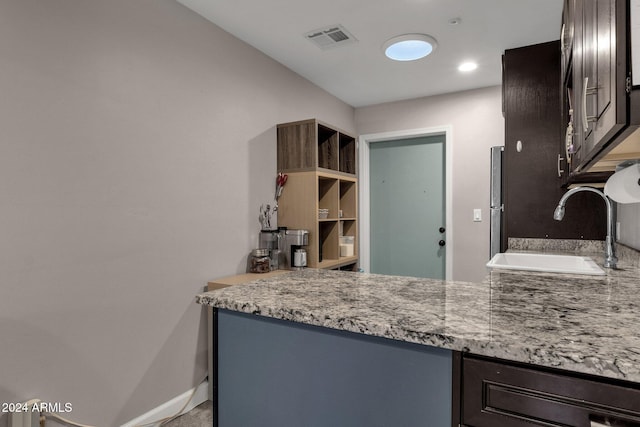 kitchen featuring light stone countertops, sink, and dark brown cabinets