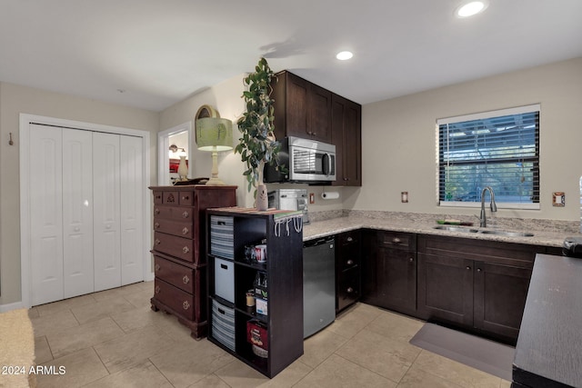 kitchen with light stone counters, dark brown cabinets, sink, light tile patterned floors, and dishwasher