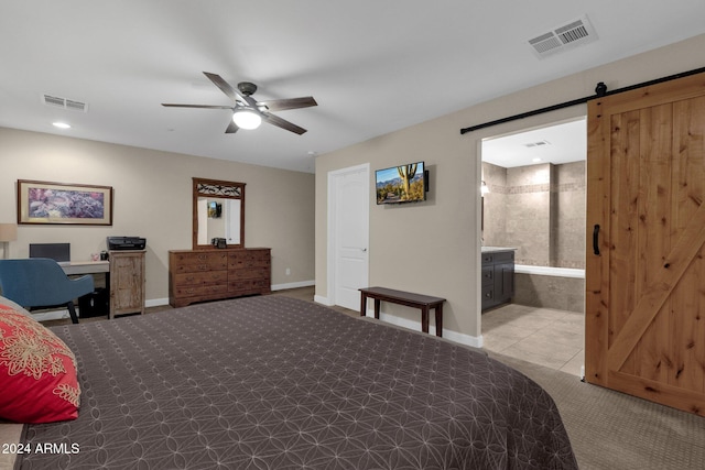 tiled bedroom featuring a barn door, ensuite bathroom, and ceiling fan