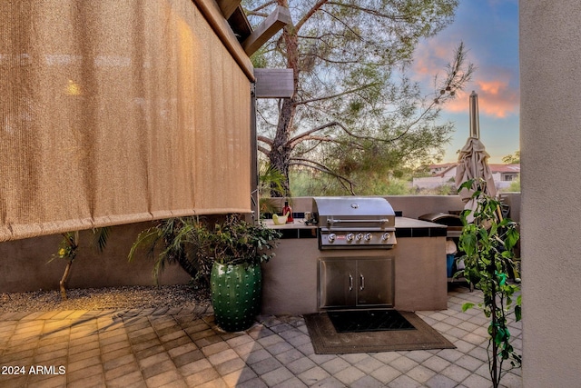 patio terrace at dusk featuring a grill and exterior kitchen