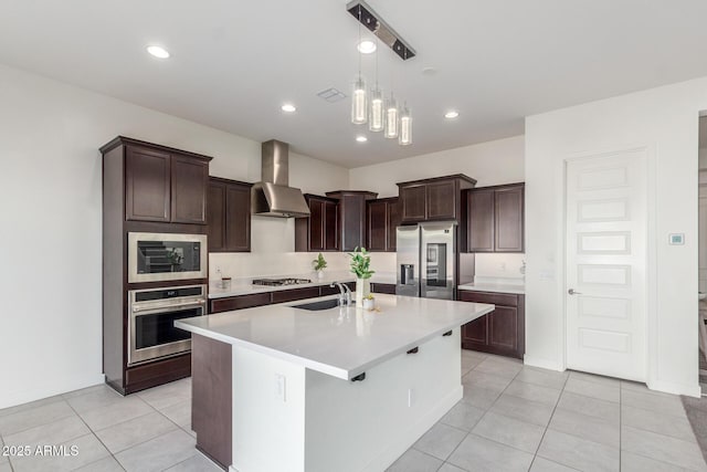 kitchen with appliances with stainless steel finishes, sink, a kitchen island with sink, light tile patterned floors, and wall chimney exhaust hood