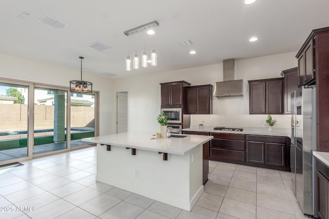 kitchen with pendant lighting, wall chimney range hood, gas stovetop, and a center island with sink