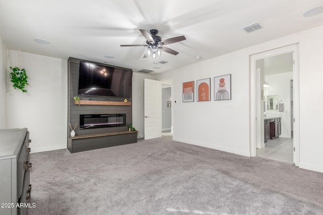 unfurnished living room featuring light colored carpet, a large fireplace, and ceiling fan