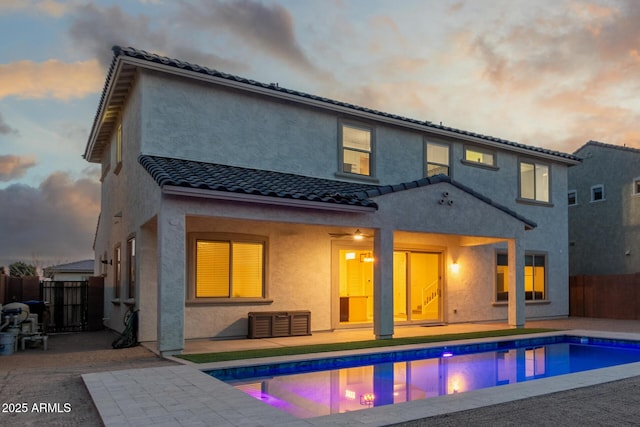 back house at dusk with a fenced in pool and a patio area