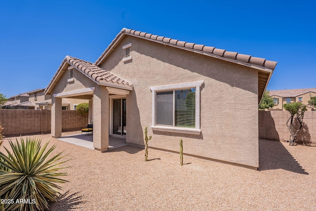 rear view of house with a patio, stucco siding, a fenced backyard, and a tiled roof