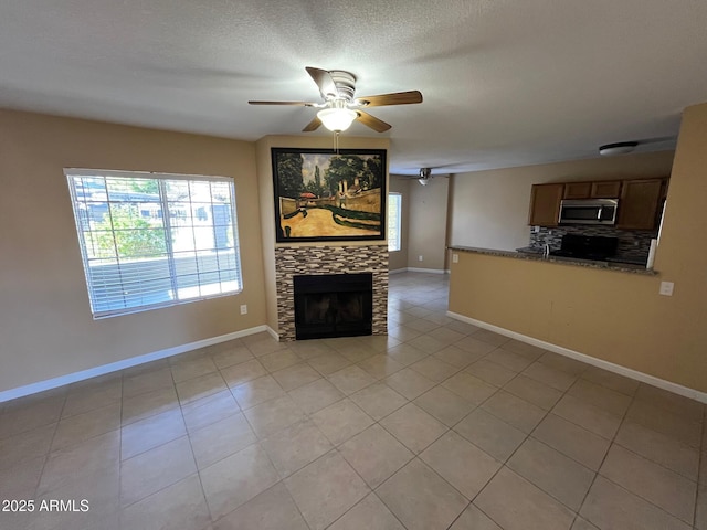 unfurnished living room with ceiling fan, light tile patterned floors, and a textured ceiling