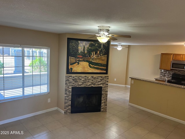 unfurnished living room with a fireplace, ceiling fan, light tile patterned flooring, and a textured ceiling