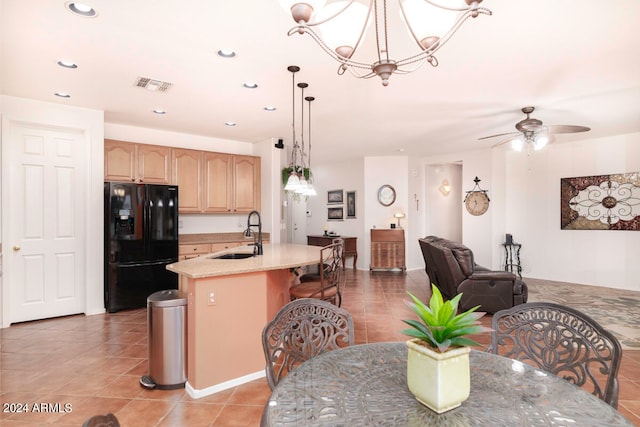 kitchen with black fridge with ice dispenser, light brown cabinets, a center island with sink, sink, and hanging light fixtures