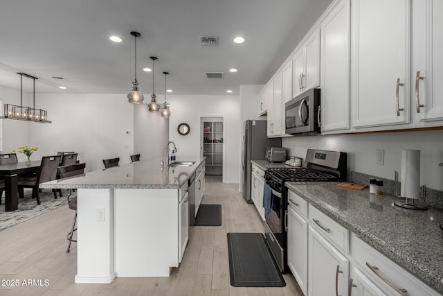 kitchen with a breakfast bar, a center island with sink, white cabinets, sink, and appliances with stainless steel finishes