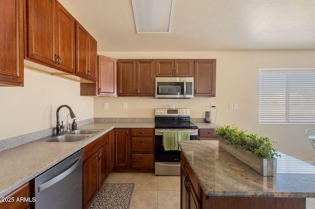 kitchen with stainless steel appliances, a center island, a sink, light tile patterned flooring, and brown cabinetry