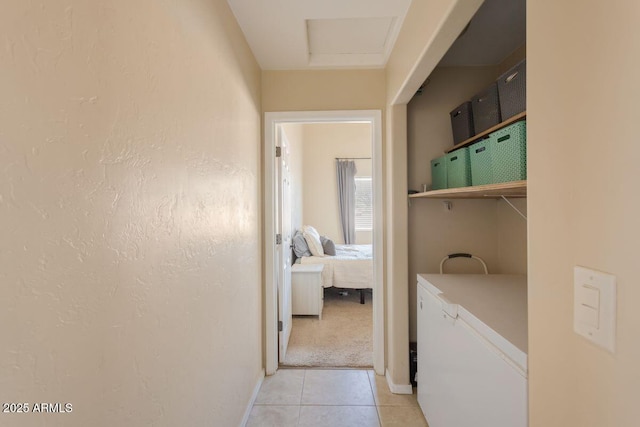 clothes washing area featuring light tile patterned flooring, a textured wall, baseboards, and attic access
