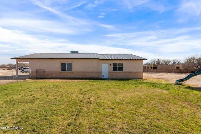 rear view of house featuring a playground, stucco siding, fence, metal roof, and a yard