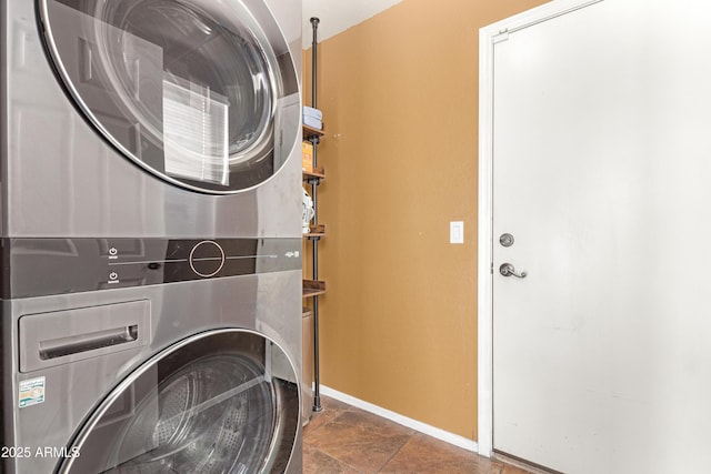 laundry room with laundry area, stone finish floor, stacked washing maching and dryer, and baseboards