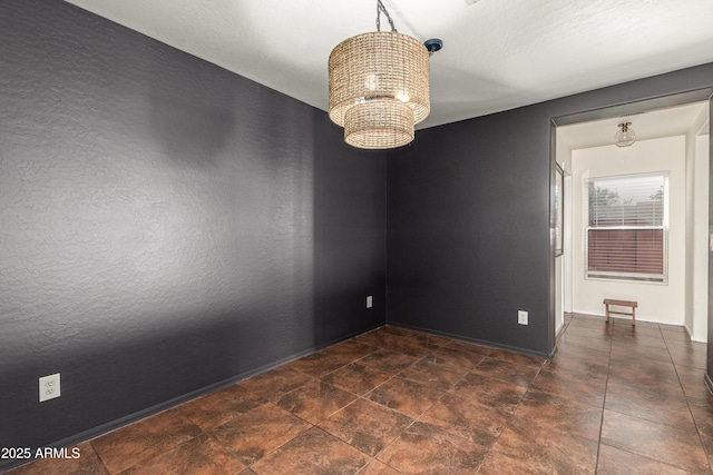 empty room featuring a chandelier, stone finish floor, and baseboards