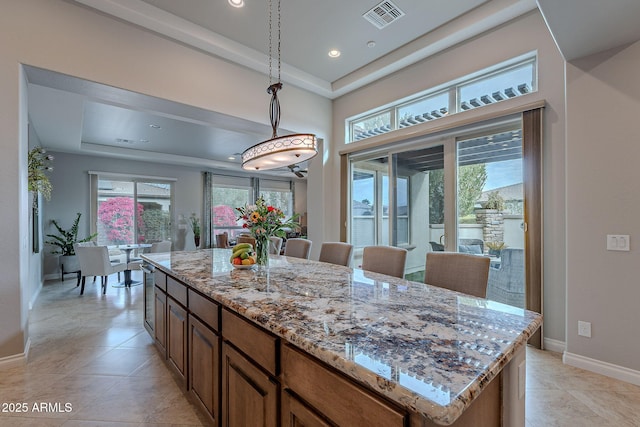 kitchen with hanging light fixtures, light stone countertops, a kitchen island, and a wealth of natural light