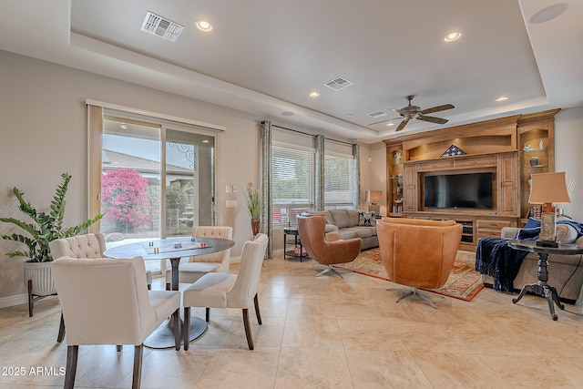 tiled dining room with ceiling fan and a raised ceiling