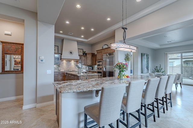 kitchen with a large island, appliances with stainless steel finishes, backsplash, light stone countertops, and decorative light fixtures