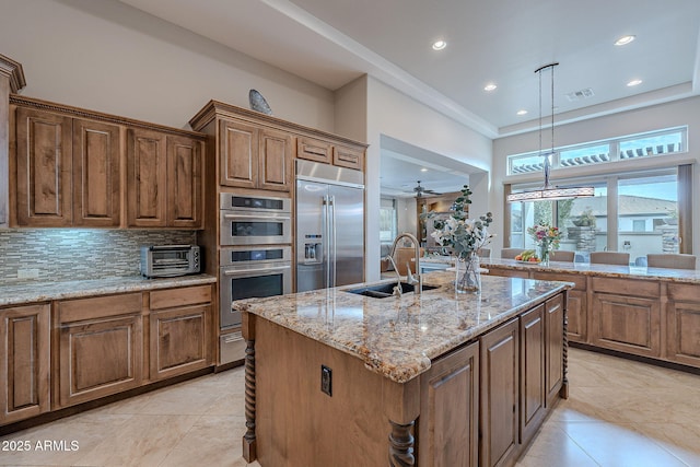 kitchen with pendant lighting, sink, appliances with stainless steel finishes, a kitchen island with sink, and light stone countertops