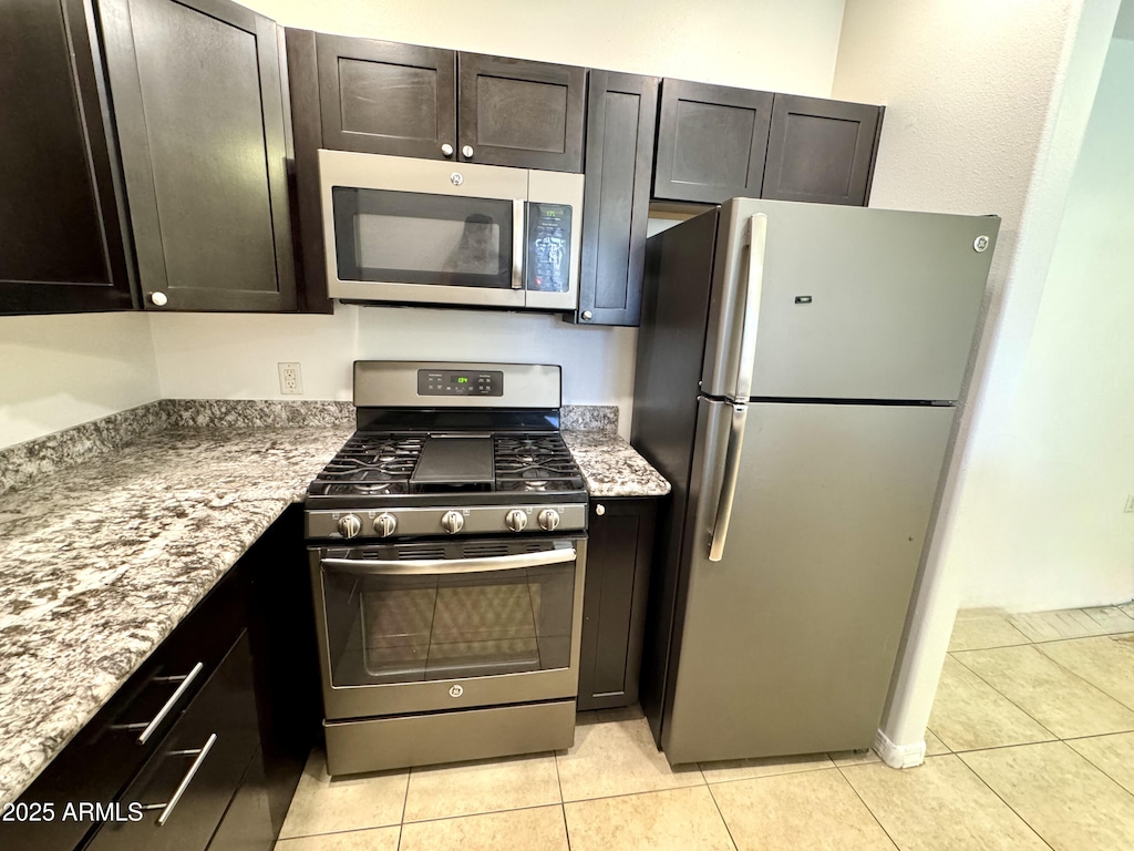 kitchen with light stone countertops, light tile patterned floors, stainless steel appliances, and dark brown cabinets