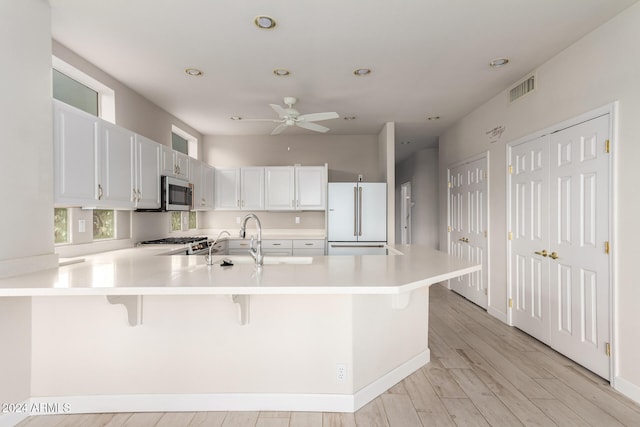 kitchen featuring kitchen peninsula, white cabinets, appliances with stainless steel finishes, a kitchen breakfast bar, and light wood-type flooring