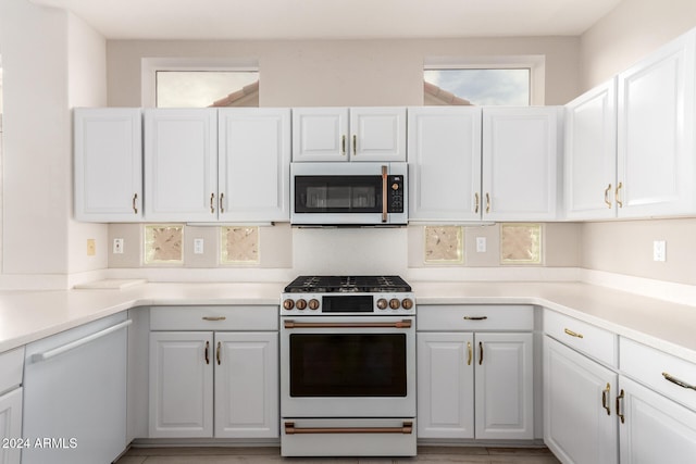 kitchen with white appliances, hardwood / wood-style flooring, and white cabinetry