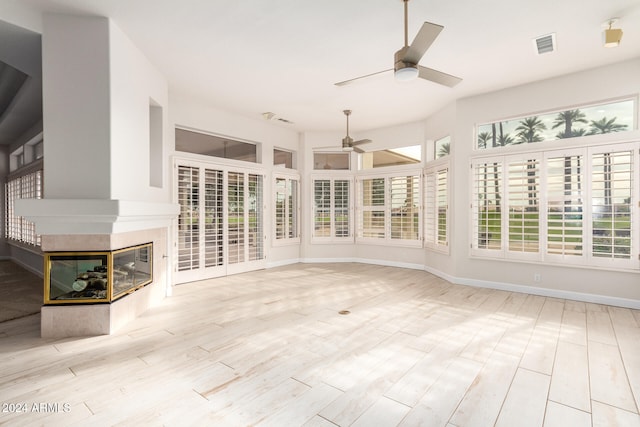 unfurnished sunroom featuring ceiling fan and a multi sided fireplace