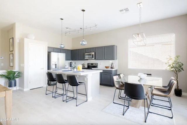 kitchen with a breakfast bar area, appliances with stainless steel finishes, a kitchen island with sink, gray cabinetry, and decorative light fixtures