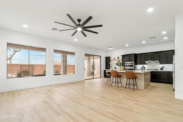 kitchen featuring under cabinet range hood, visible vents, an island with sink, and light countertops