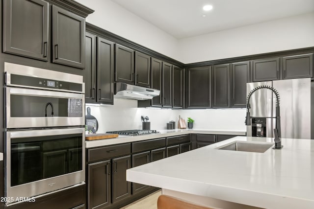 kitchen with light stone counters, recessed lighting, a sink, stainless steel appliances, and under cabinet range hood