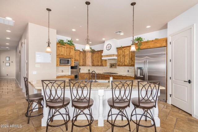 kitchen featuring a large island with sink, light tile patterned floors, hanging light fixtures, decorative backsplash, and built in appliances