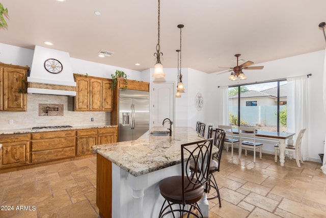 kitchen with stainless steel appliances, light tile patterned floors, custom range hood, decorative backsplash, and an island with sink