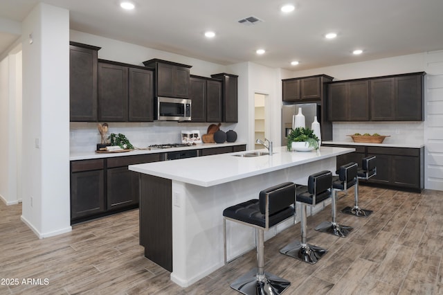 kitchen featuring a breakfast bar, a center island with sink, sink, dark brown cabinets, and stainless steel appliances