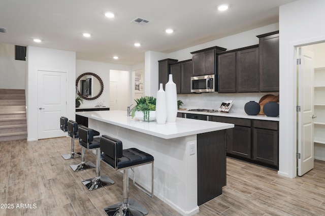 kitchen with decorative backsplash, dark brown cabinets, stainless steel appliances, a kitchen island with sink, and a breakfast bar area