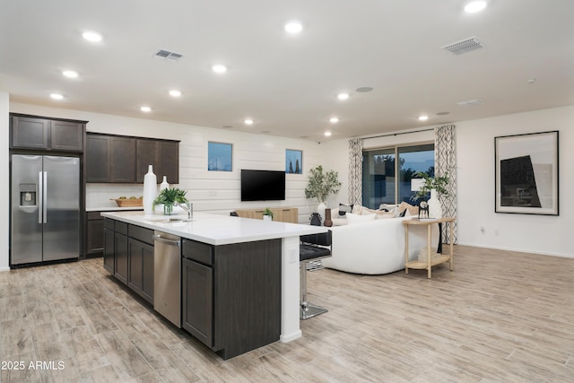 kitchen with a kitchen breakfast bar, sink, light wood-type flooring, an island with sink, and stainless steel appliances