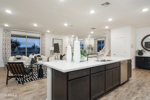 kitchen with dishwasher, dark brown cabinetry, a center island with sink, and sink