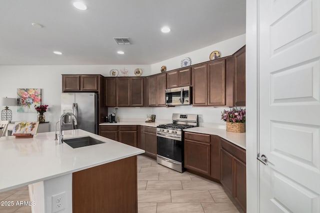 kitchen with stainless steel appliances, an island with sink, dark brown cabinets, and sink