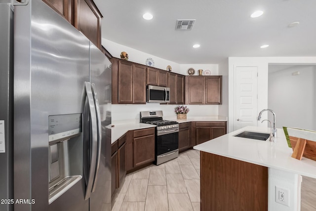 kitchen with dark brown cabinetry, sink, an island with sink, and appliances with stainless steel finishes