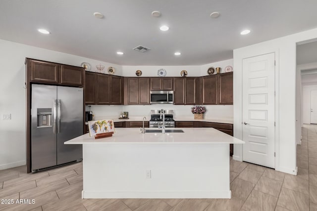 kitchen with dark brown cabinets, stainless steel appliances, and a center island with sink