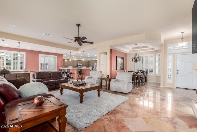 living area featuring a tray ceiling, recessed lighting, ceiling fan with notable chandelier, baseboards, and visible vents
