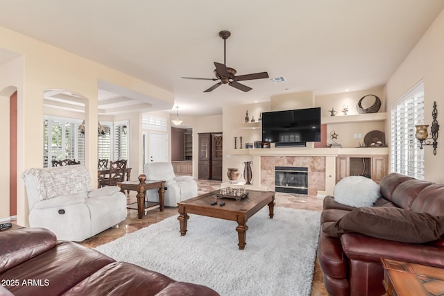 living area with a high end fireplace, visible vents, arched walkways, and ceiling fan