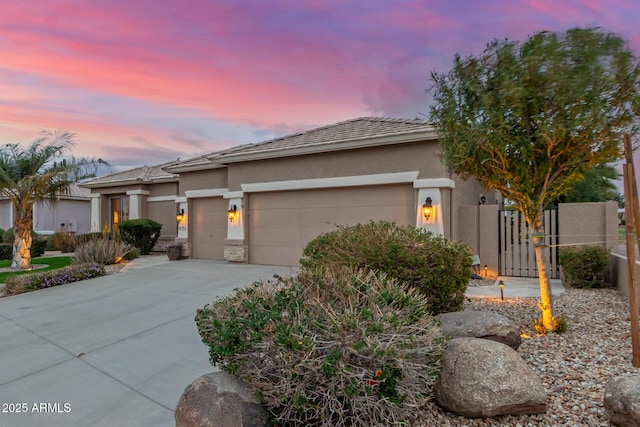 view of front facade featuring stucco siding, concrete driveway, an attached garage, and a gate