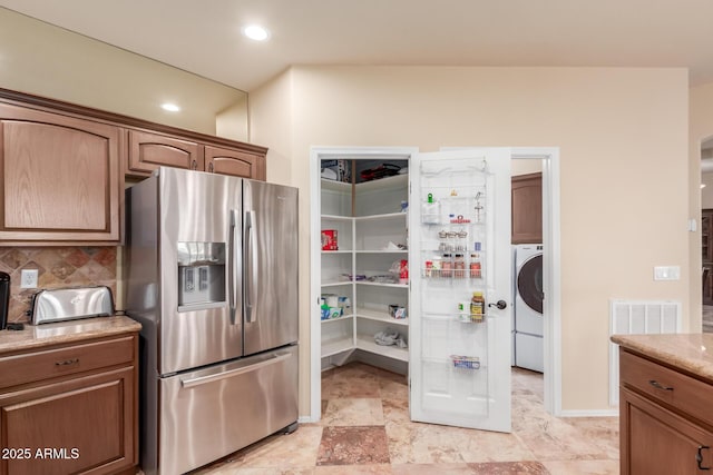 kitchen featuring stainless steel fridge, tasteful backsplash, washer / clothes dryer, light stone counters, and brown cabinets