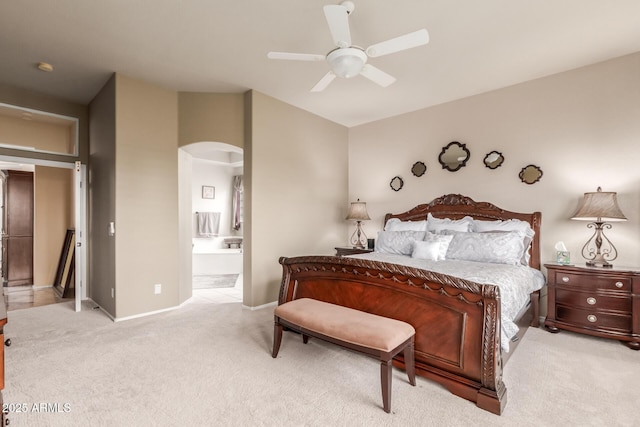 bedroom with a ceiling fan, baseboards, ensuite bath, light colored carpet, and arched walkways