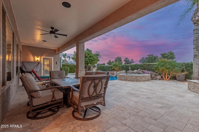 patio terrace at dusk featuring an in ground hot tub, ceiling fan, and a fenced in pool