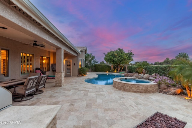 pool at dusk featuring a fenced in pool, an in ground hot tub, a patio area, and a ceiling fan