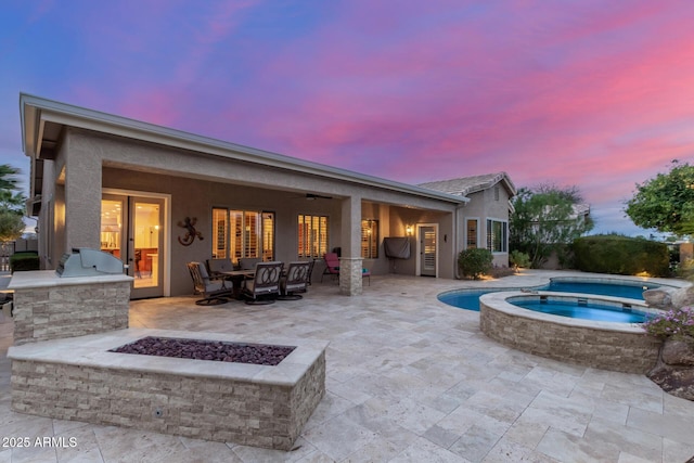 pool at dusk with a fire pit, a pool with connected hot tub, a patio area, area for grilling, and ceiling fan