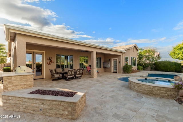 rear view of property featuring stucco siding, exterior kitchen, a ceiling fan, an in ground hot tub, and a patio area