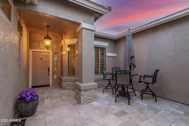exterior entry at dusk with outdoor dining space, stucco siding, and a patio area